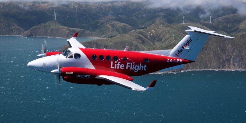 Life Flight Plane Flying over sea with hills and clouds in the background.