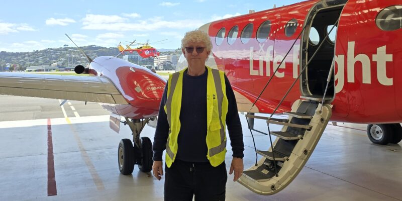Paul standing in front of Life Flight Air Ambulance Plane with Life Flight Westpac Rescue Helicopter flying in background.